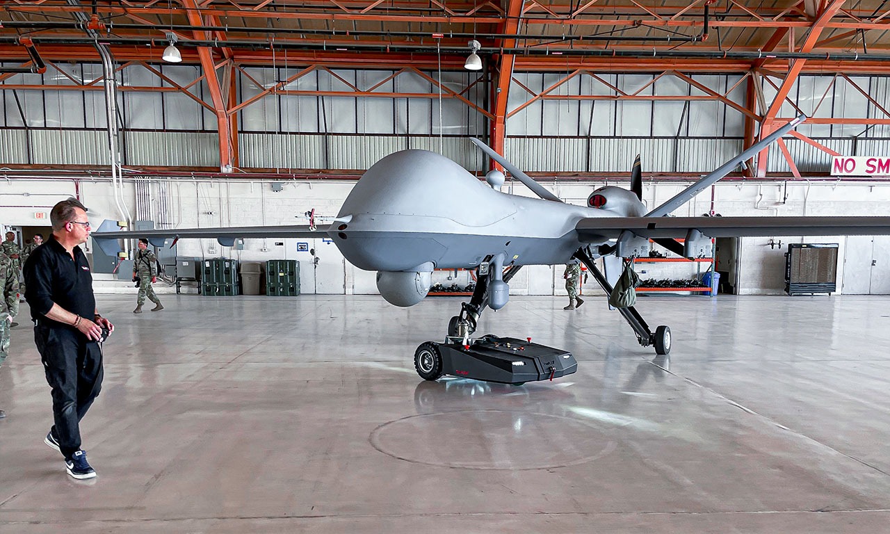 Electric TowFLEXX TF3 Milspec tug towing a MQ-9 Reaper drone of the United States Air Force on a military base, showcasing innovative ground support technology for unmanned aerial vehicles.